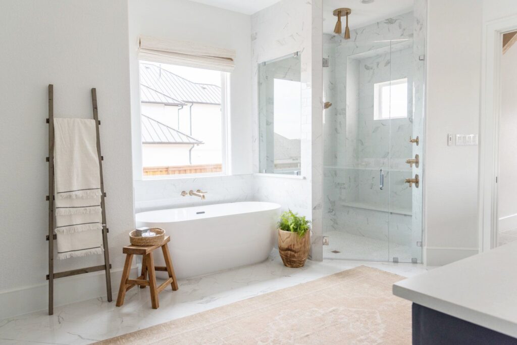 A view of a bathroom with beachy look and a glass door with a linen hanging and a white tub