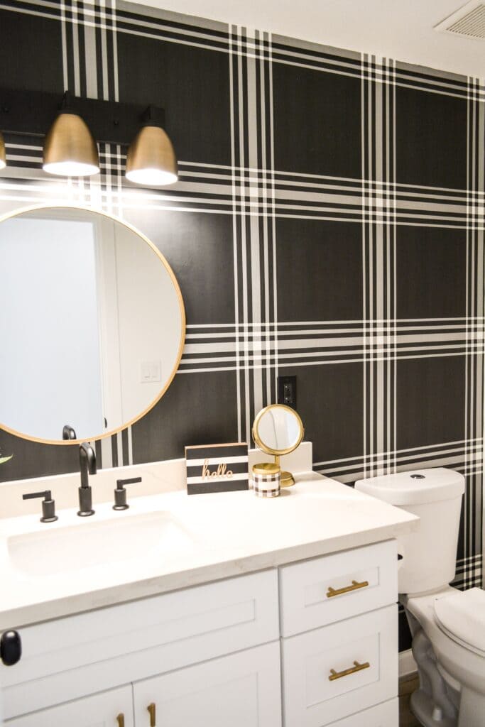 A view of a black and white plaid wallpaper over a white bathroom sink with a round mirror