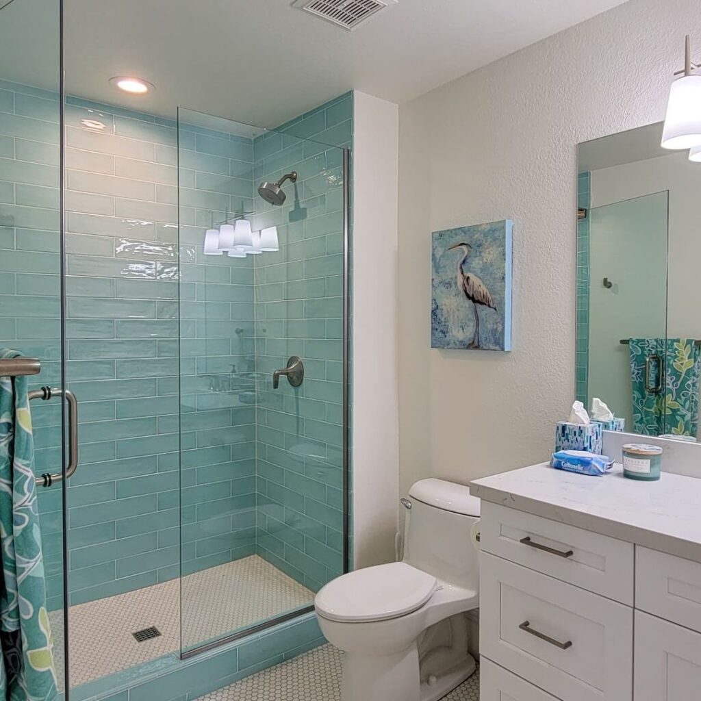 A view of a blue glass shower and white cabinets in a beachy bathroom