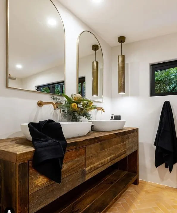 A view of a earthy shade wooden cabinet placed under the sink with glam mirrors in a bathroom