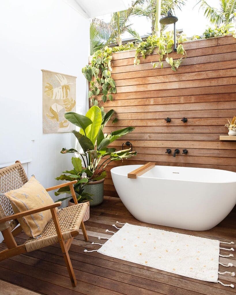 A view of plants in a bathroom woith white sink and a jute chair and a white mat with wooden floor