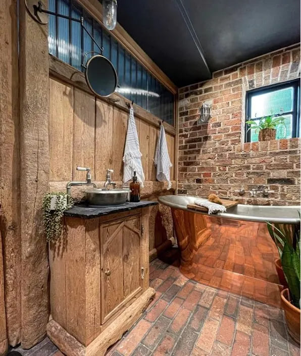A view of rustic wooden bathroom with brick floor tiles and walls and a copper tub