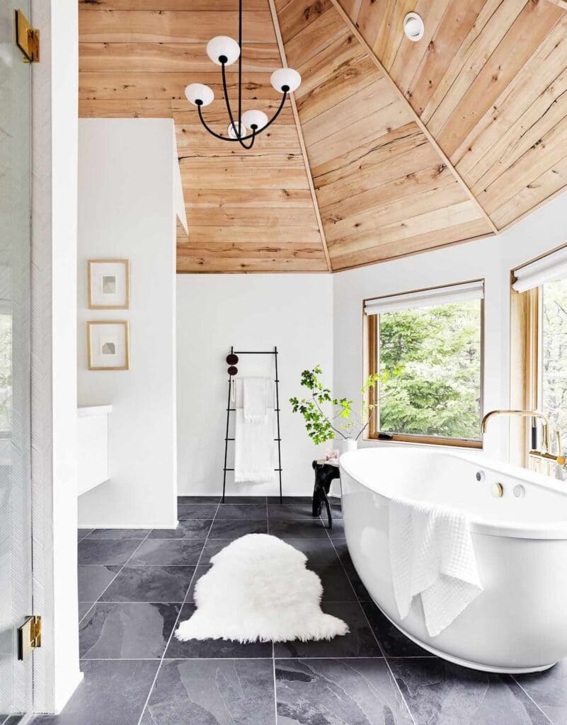 A view of wooden clad in the ceiling of an open bathroom with a tub and window