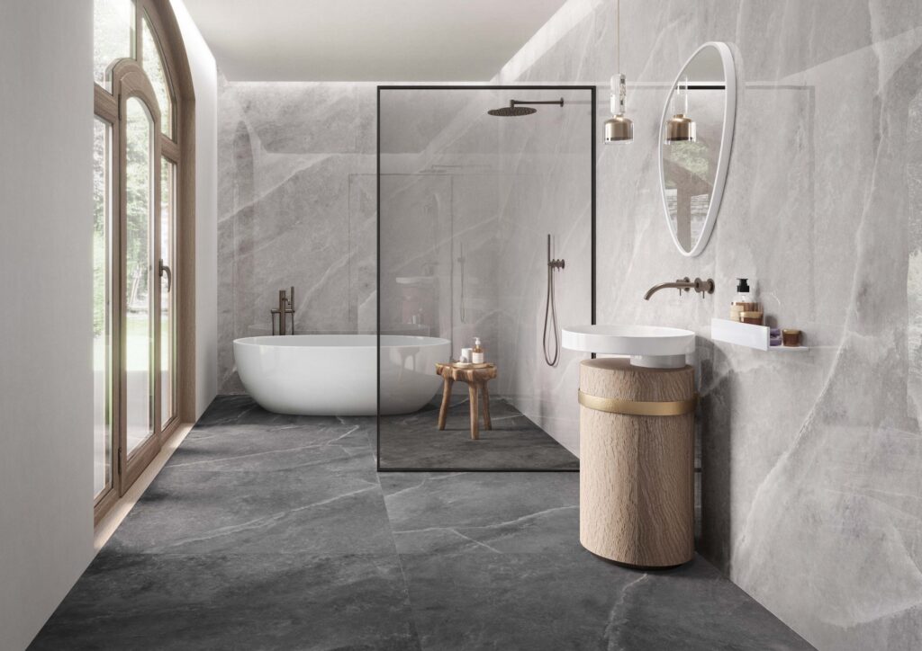 gray colored large bathroom tiles in a small master bathroom white bathtub an oval shaoed mirror sink and pocket door