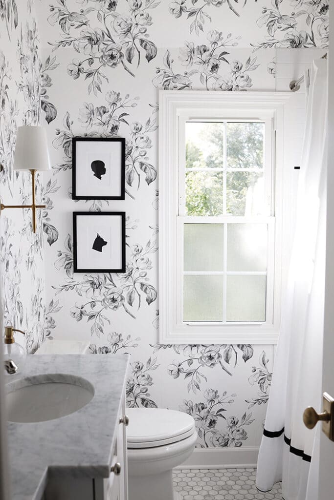 black and white floral wallpaper on the walls of bathroom, art pieces hung on the wall