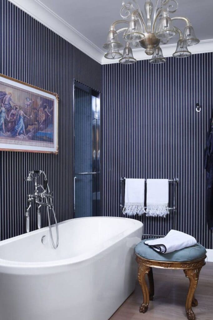black and white stripes on walls in bathroom a white bathtub stool and towells