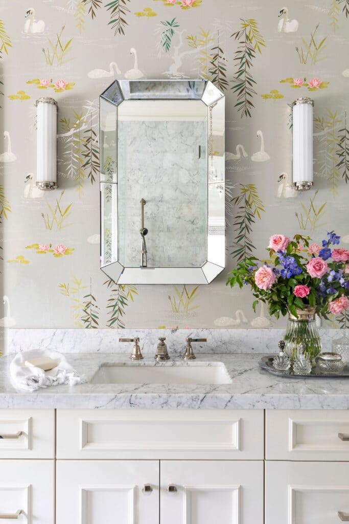 textured floral wallpaper with a mirror lighting fixtures on the wall flowers in a vase placed on sink