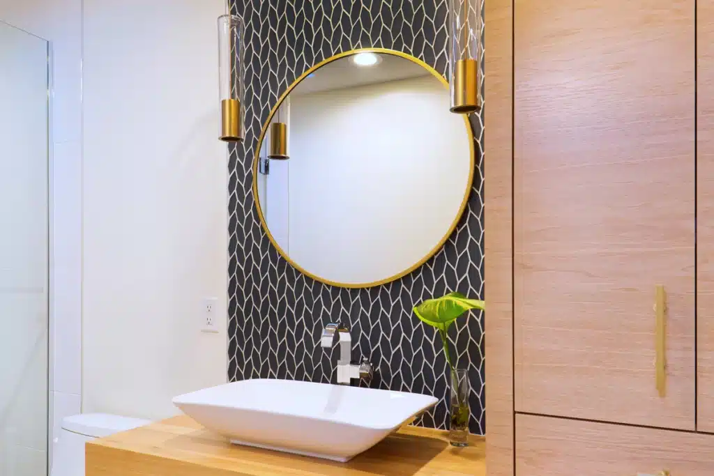 A view of a gold rimmed round bathroom mirror over the sink