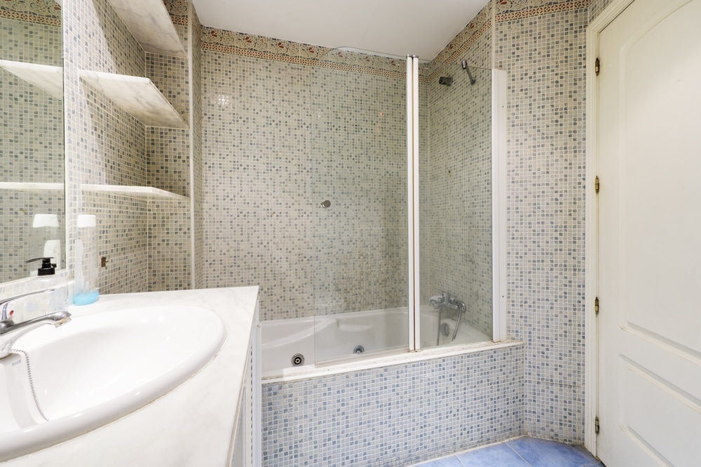 Bathroom with white porcelain sink, marble countertop, chrome taps, frameless mirror, white shower tray and tiled walls with stoneware