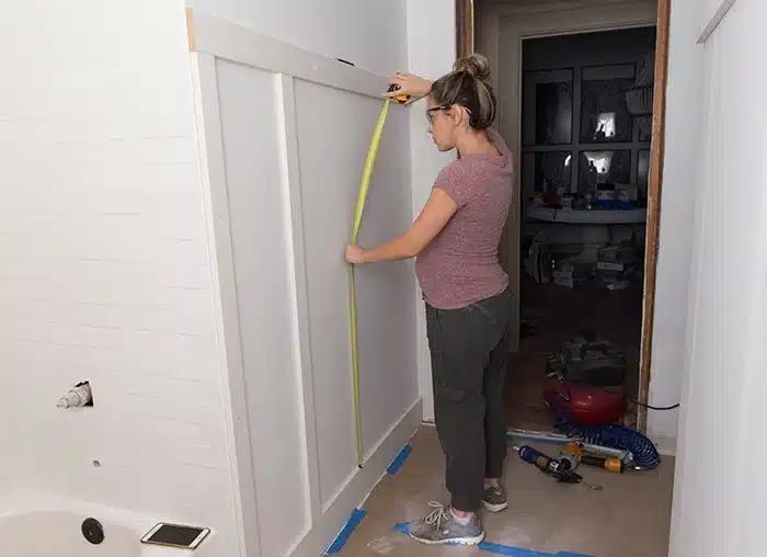 a lady measuring the wall using a measuring tape in bathroom other materials on the ground