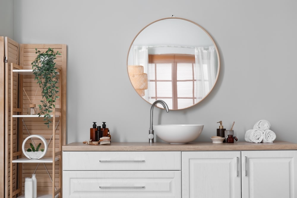 grey color on wall of bathroom roundmirror and toiletries on the sink